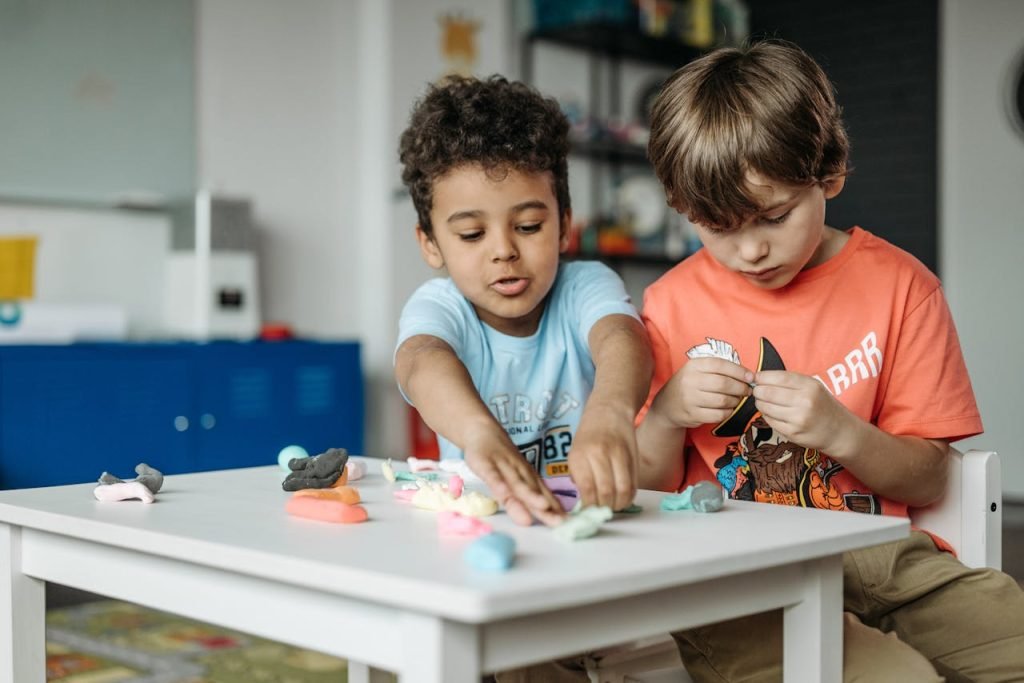 Two children playing and crafting with clay at a table in a kindergarten classroom.